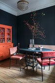 Black table with velvet chairs and coral-colored sideboard in the dining area with black walls