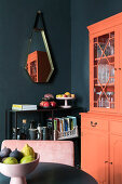 Coral-colored sideboard and black shelf in the dining area with black walls