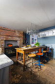 Industrial table with vintage bar stools, in front of a brick wall with a stove in the kitchen