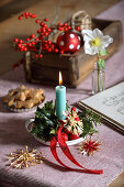 Christmas table decoration with candle, straw stars, holly and Christmas rose