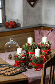 Advent wreath with greenery, red ribbon decorations and cookies on a rustic table