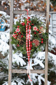 Winter wreath made from fir branches, straw stars and red berries on a wooden ladder