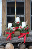 Weihnachtliche Kerzendekoration mit roten Schleifen auf Holzbank vor Fenster