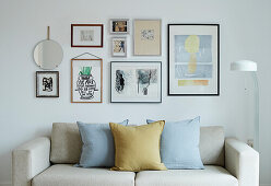 Pale sofa with scatter cushions below gallery of pictures on wall