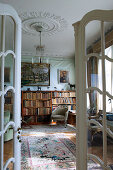 A view through open French doors into a music room with a bookshelf and an antique chandelier