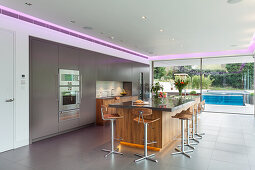 An elegant fitted kitchen with indirect lighting and a kitchen island with bar stools