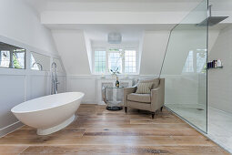 Freistehende Badewanne, Beistelltisch und Sessel, Dusche hinter Glastrennwand in hellem Badezimmer