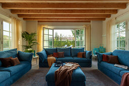 Blaue Polstergarnitur vor geöffneter Terrassentüre im Zimmer mit Holzbalkendecke