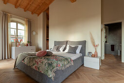 A double bed with a grey cover, pillows and a bedspread in a bedroom with an ensuite bathroom in the background