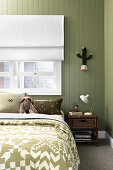 Doppelbett unter Fenster im Schlafzimmer mit grün gestrichener Holzwand