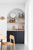 Kitchen base cabinets and shelves in an arched wall niche, dining table, and chair in foreground