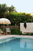 Pool mit Liegestühlen und Sonnenschirm, im Hintergrund üppige Vegetation