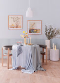 Runder Tisch mit bodenlanger Tischdecke und Stühle im Zimmer in Pastell- und Erdtönen