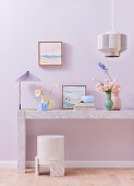 Marble console with decorative objects and flowers in front of wall in pastel lilac