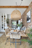 Dining table, woven pendant light above in front of brick wall