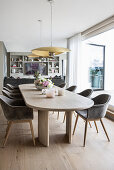 Long dining table in light wood with elegant, upholstered shell chairs in front of a patio door