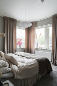 Double bed with bedspread in front of window with curtains in rosé