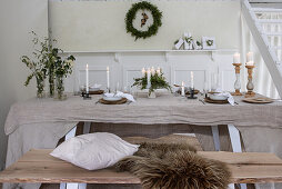 Festlich und weihnachtlich gedeckter Esstisch mit Kerzen und Kranz an der Wand