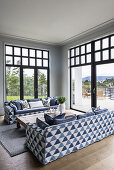 Sofas with blue and white upholstery and wooden coffee table in light-flooded room with French windows