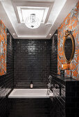 Bathtub in bathroom with black wall tiles and wallpaper in orange tones