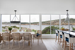 Dining area and kitchen island in front of wall of windows, view of coastal landscape