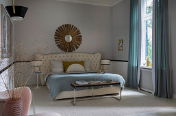 Double bed with high, cushioned headboard in bedroom with light grey walls