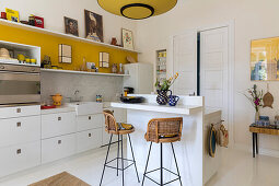 Bright kitchen with breakfast bar and vintage rattan bar stools, yellow stripe on the wall