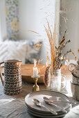 Herbstlich dekorierter Tisch mit Tellerstapel, Trockengräsern, Kerze und Krug