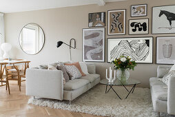 Helle Sofas, Glastisch und Bilder an beigefarbener Wand in offenem Wohnraum