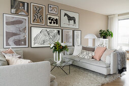 Light sofas, glass table and pictures on beige-coloured wall in open-plan living room