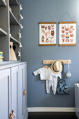 Children's clothing hanging on hooks, pictures with animal motifs on blue-grey wall above hooks