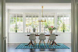 Verglaste Veranda mit Esstisch und weißen Klassikerstühlen auf türkisblauem Teppich
