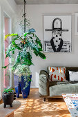 Zimmerpflanze neben dem Sofa, darüber moderne Kunst in sonnenbeschienenem Wohnzimmer
