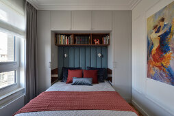 Doppelbett mit gepolsterter Platte am Kopfteil, darüber Bücherregal und raumhoher Einbauschrank