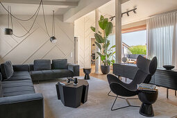 Eleganter Wohnraum mit dunkler Sofagarnitur, schwarzem Couchtisch und Klassiker-Loungesessel