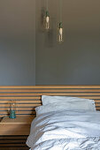 Doppelbett mit Bettkopftteil aus Holz und integriertem Nachttisch, darüber elegante Pendelleuchten