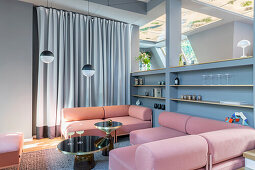 Pink sofa with elegant, black side tables and shelving wall in open-plan living room