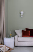 Weißer Beistelltisch neben hellem Sofa, darüber Leuchte an grüner Wand