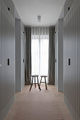Changing room with floor-to-ceiling built-in wardrobes, wooden stools in front of window in background
