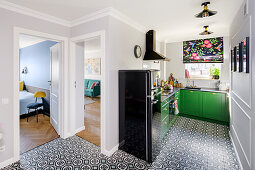Dunkelgrüne Unterschränke, schwarzer Kühlschrank und geometrische Bodenfliesen in offener Küche