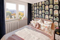Schlafzimmer mit rosa Doppelbett, Nachttisch und Tapete mit Terrarium-Motiv, Fenster mit schwarzen Samtvorhängen