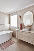 Modern Scandi style bathroom in beige tones with curved sink on top of a stone top vanity and free-standing bathtub