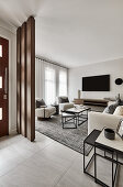 Eingangsbereich in neutralen Tönen, Blick in Lounge-Bereich mit cremefarbenen Sofas und Couchtischen aus Stein und Metall