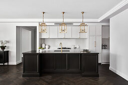 Kitchen in white and with dark Shaker-style wooden cabinets, gold lantern lighting, and gold hardware