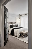 Opulentes Schlafzimmer in neutralen Tönen mit getäfelten Wänden, hängenden Kronleuchtern und französischen Türen