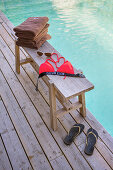 Holzbank am Pool mit Handtüchern und Sommeraccessoires