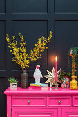 Farbenfrohes Sideboard mit Dekoration und Pflanzen vor dunkler Wand