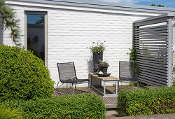 Moderne Terrassenlounge mit schwarzen Stühlen und Spalier, auf Holzdeck