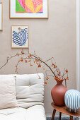 Vase with twigs and small orange berries next to cream-colored sofa