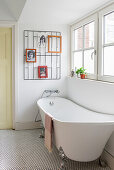 Freestanding bathtub under windows in light-colored bathroom with wall decor